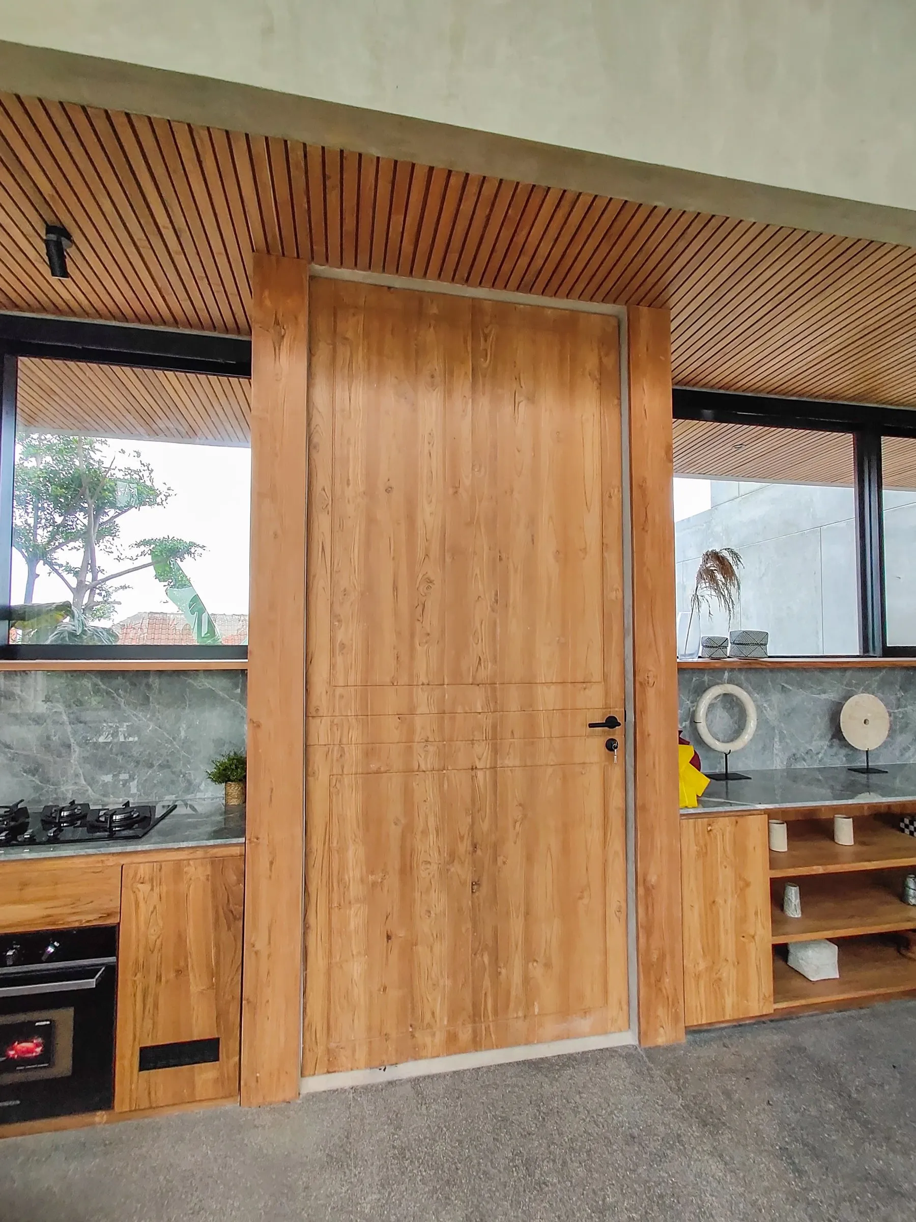 Full-height solid teak door with teak frame, set under the slatted ceiling.