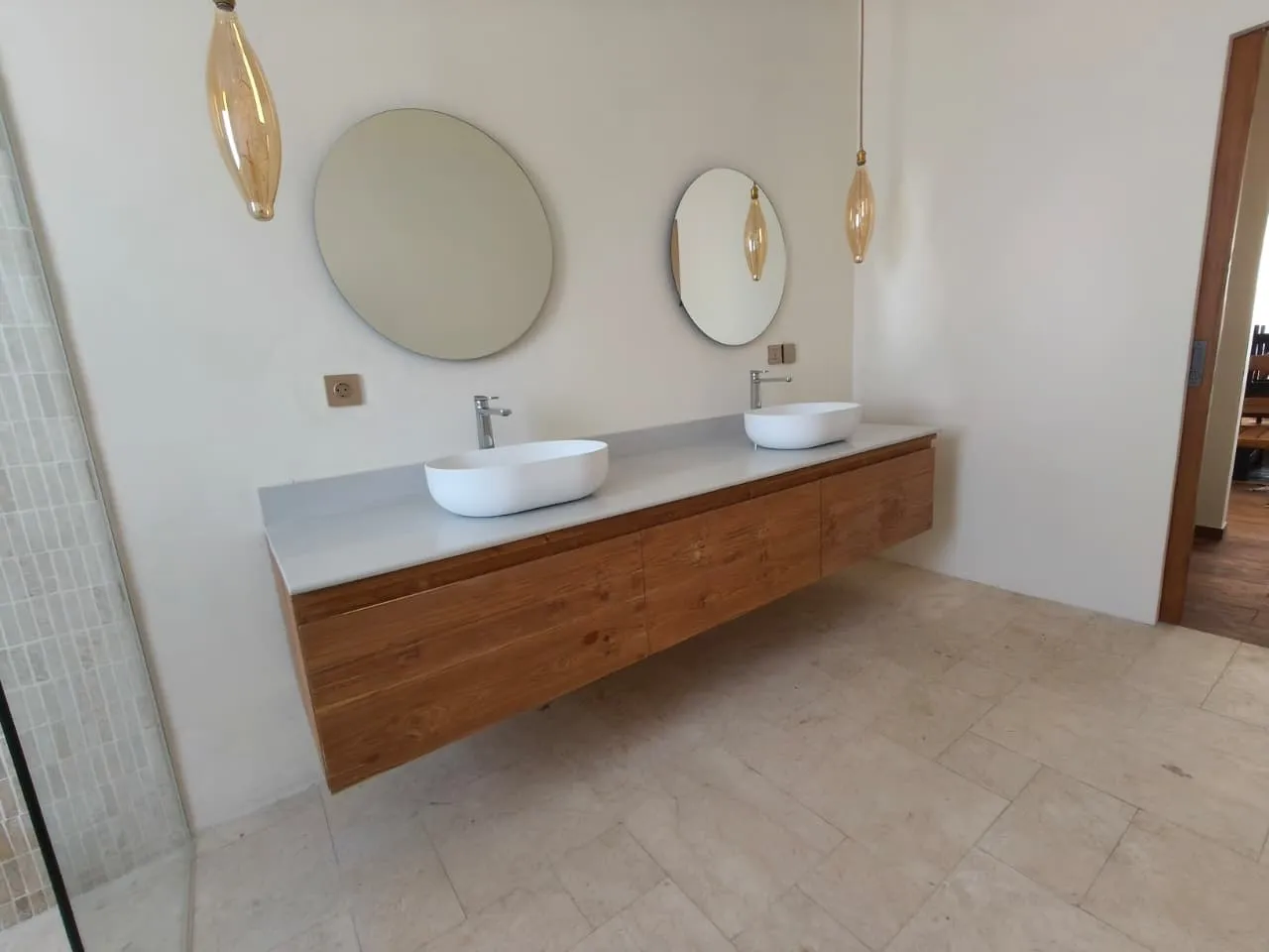 Floating teak vanity with two basins and round mirrors.