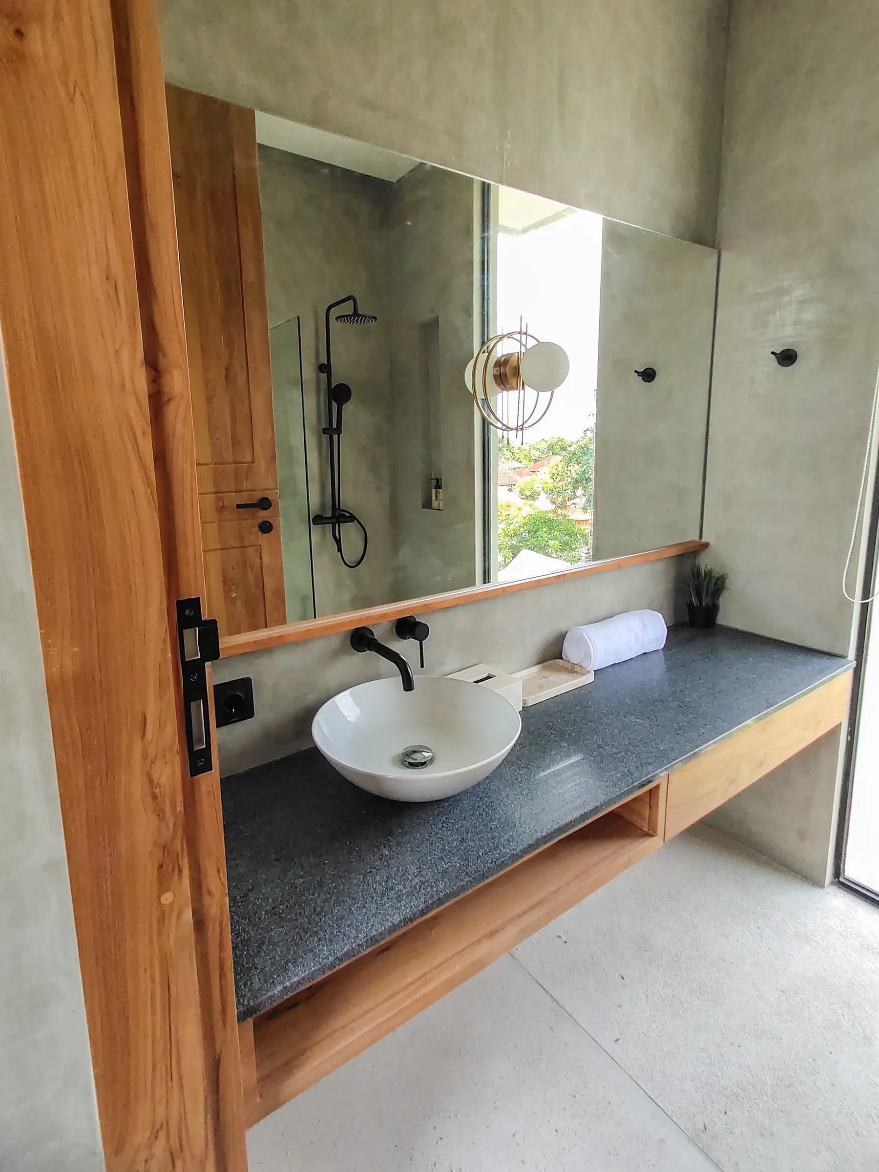Floating teak vanity with a dark stone top and vessel basin.
