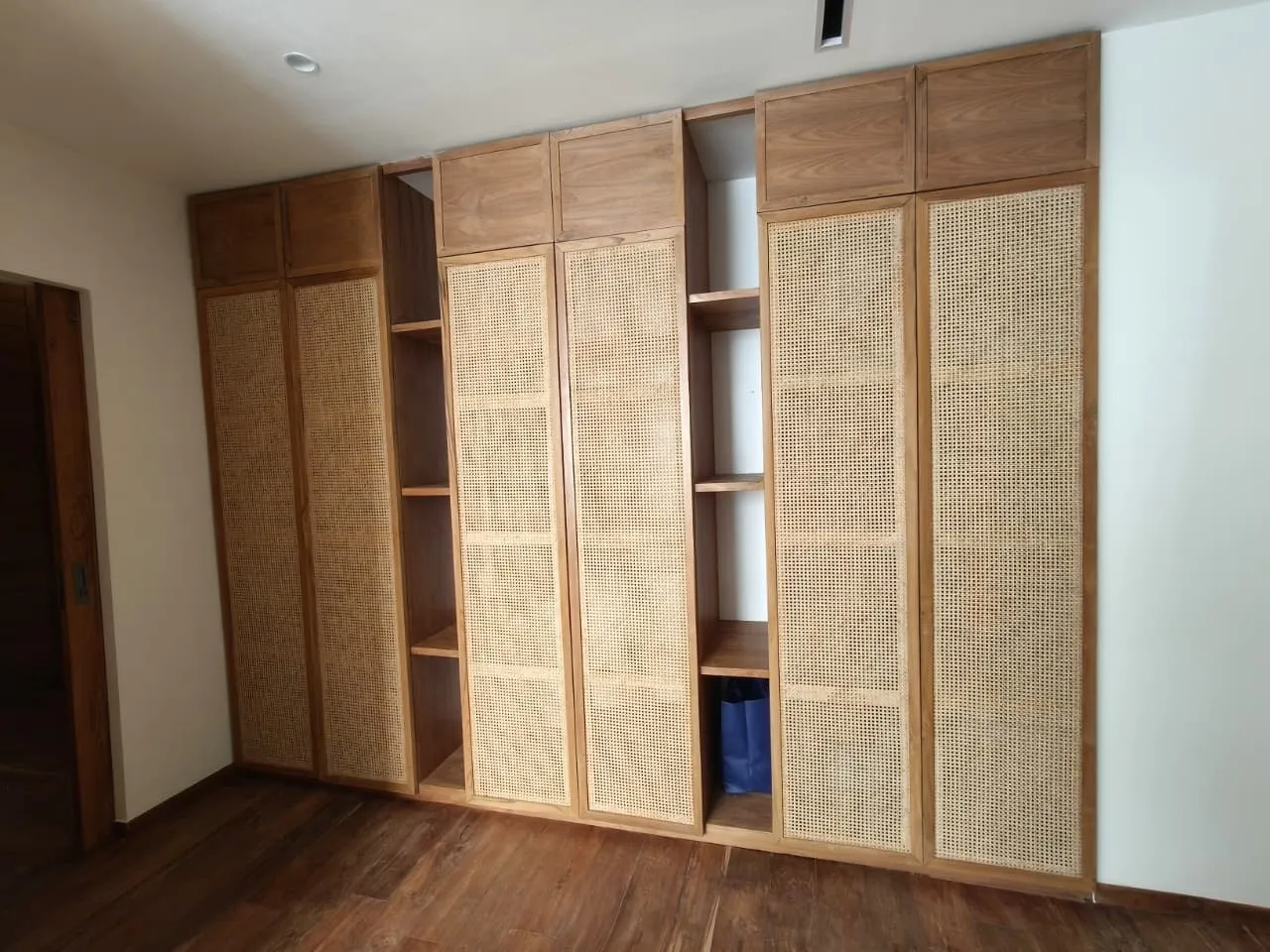 Wall of teak wardrobes with rattan door panels.